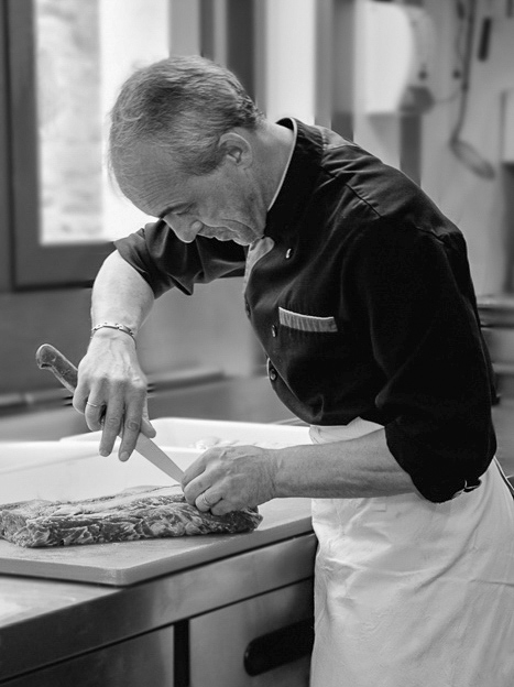 Photographie en entreprise de restauration d'un cuisinier travaillant au couteau une pièce de viande.